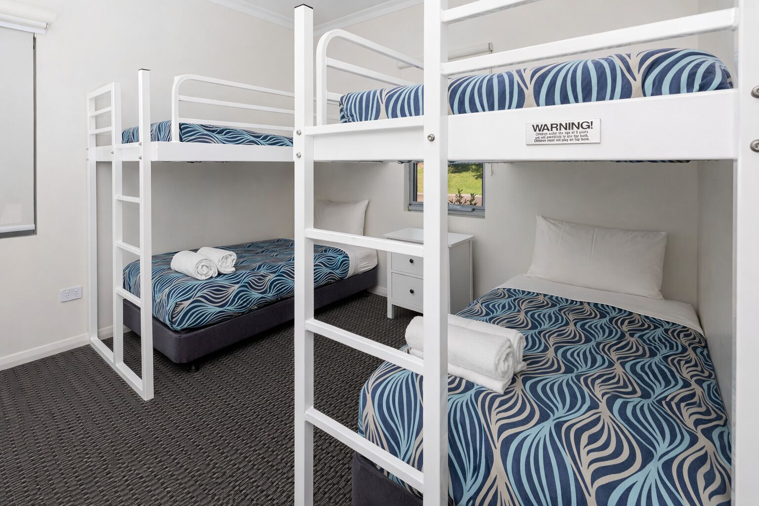 Een slaapkamer met stapelbedden, een waarschuwingstickker, een bureau en een raam met uitzicht.