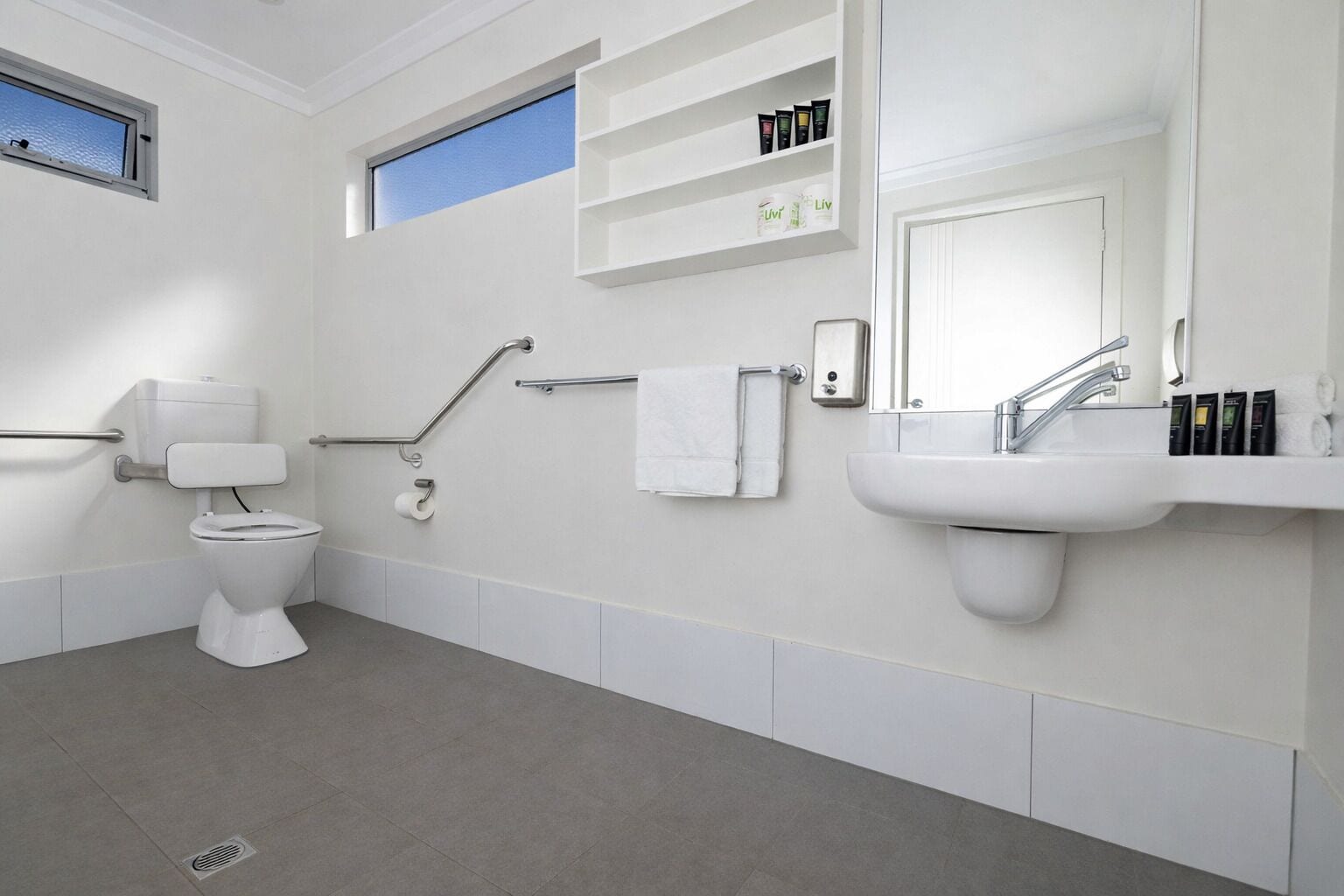 Une salle de bain moderne équipée de toilettes, d’un bidet, d’un lavabo et d’étagères où sont rangés les articles de toilette.