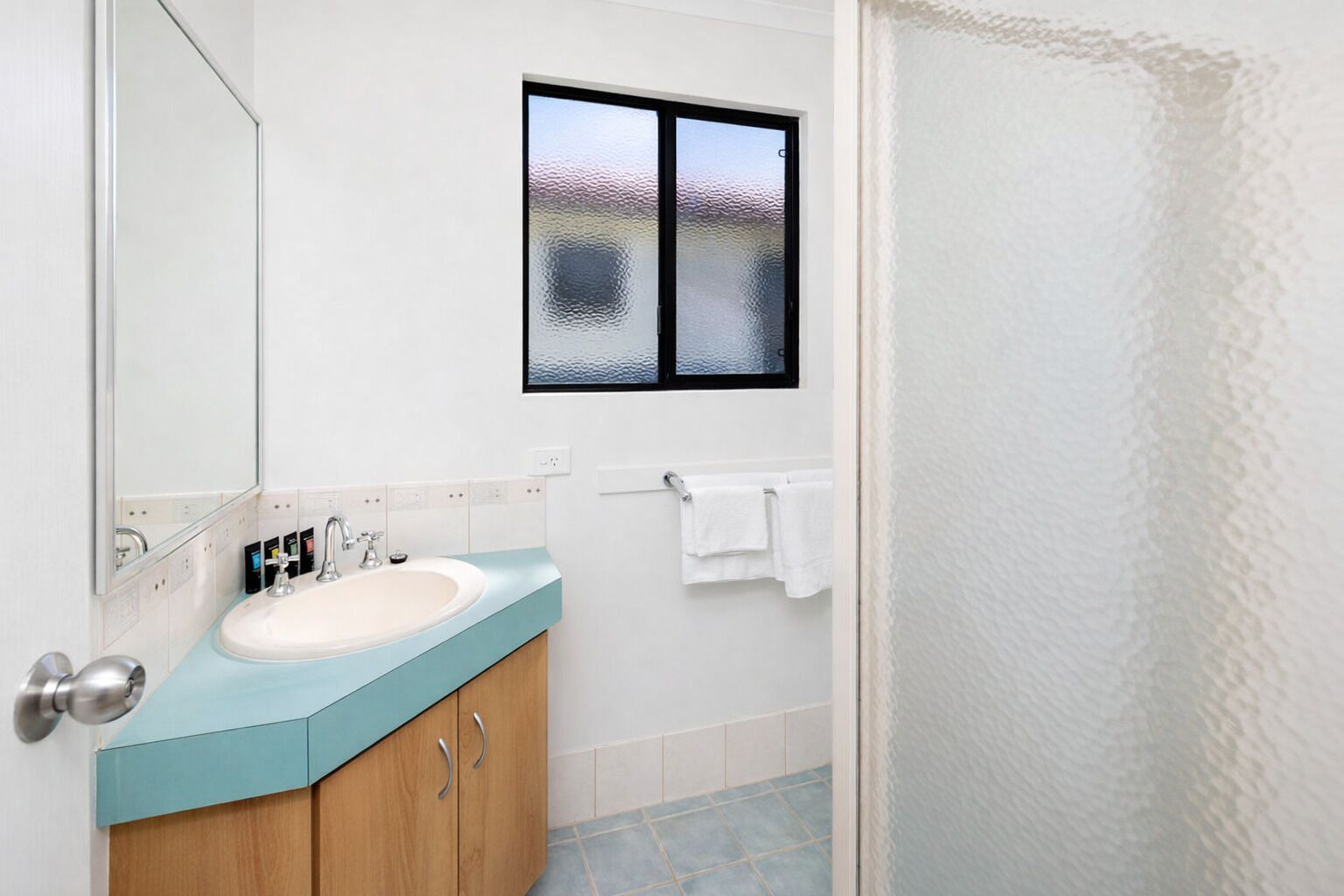 Un baño con lavamanos, espejo, ventana y toallero.