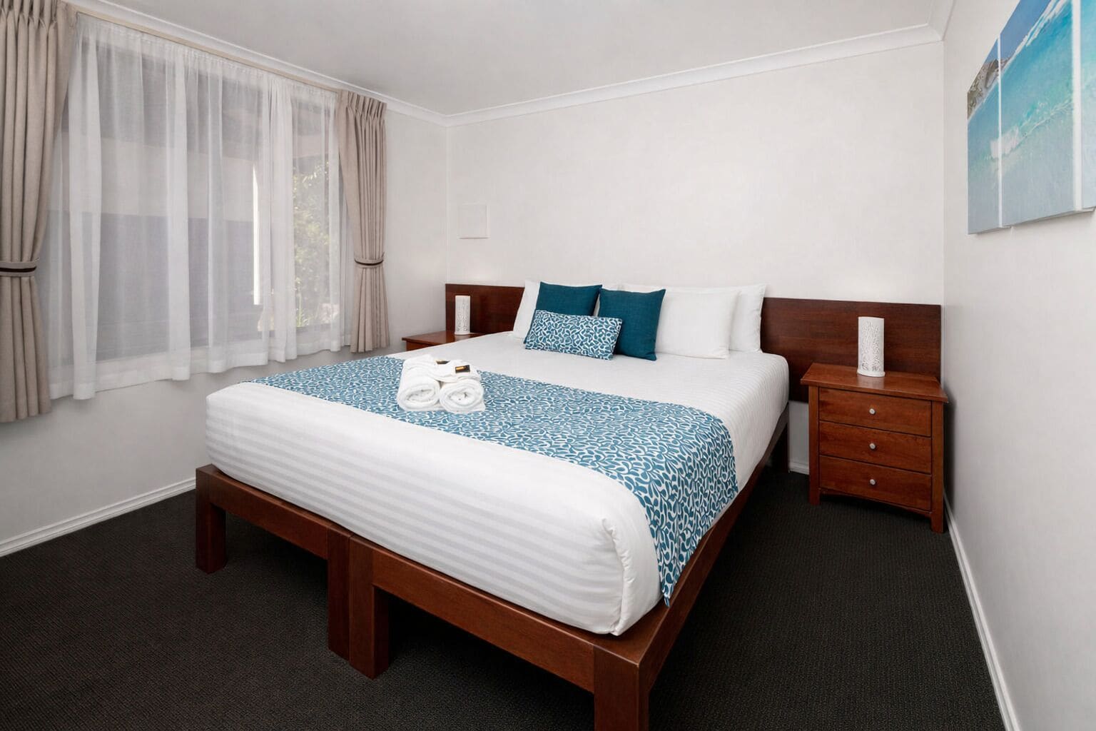 A hotel room with a large bed, a wooden nightstand, a bedside table, and a window with curtains.