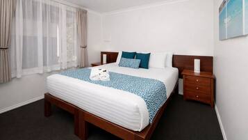 A hotel room with a large bed, a wooden nightstand, a bedside table, and a window with curtains.