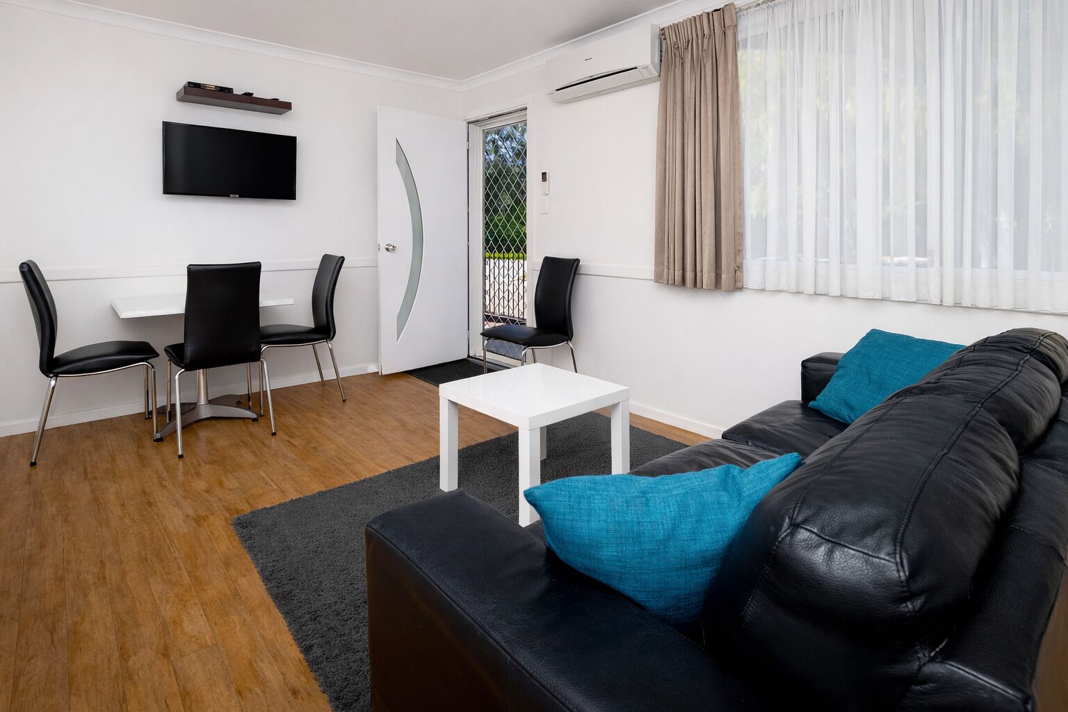 Een moderne woonkamer met een zwarte leren bank, een witte salontafel en een aan de muur bevestigde televisie.