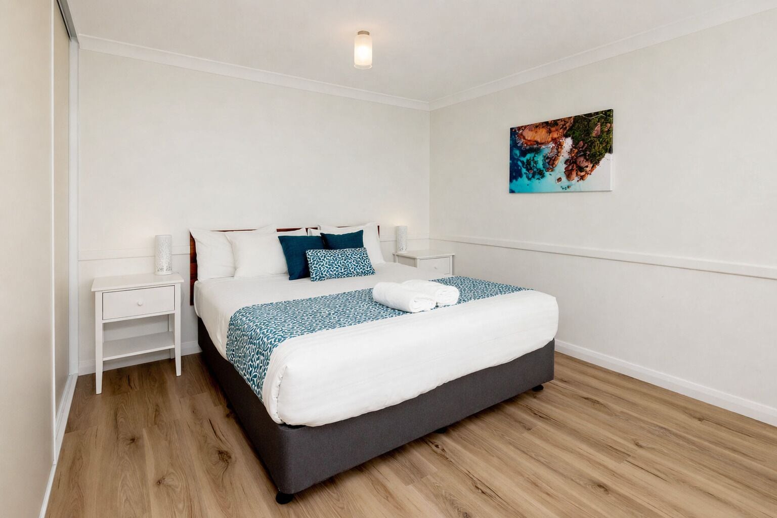 A neatly arranged bedroom with a bed, bedside tables, and a painting on the wall.