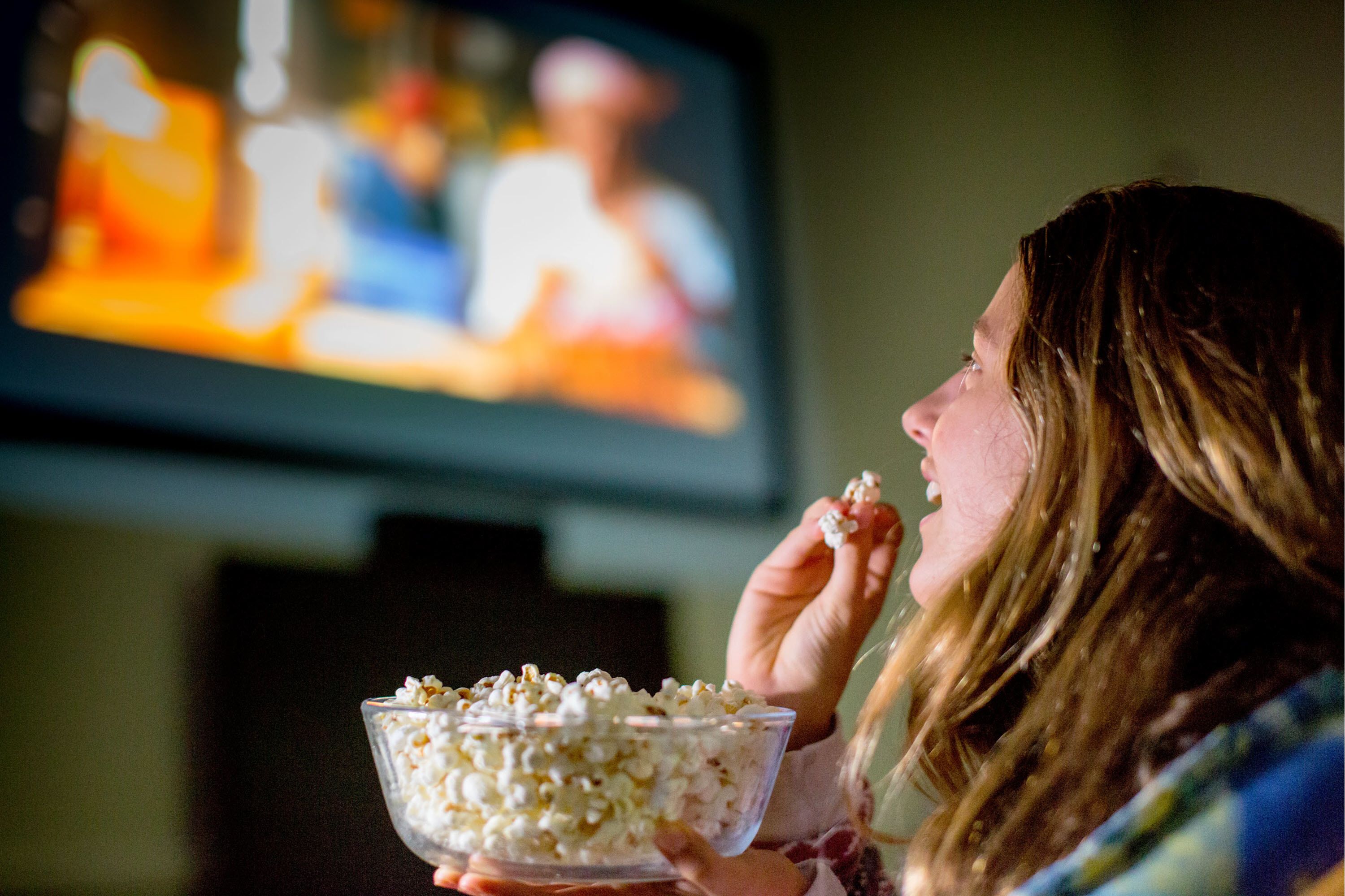 A person holding a bowl of popcorn in front of a television.