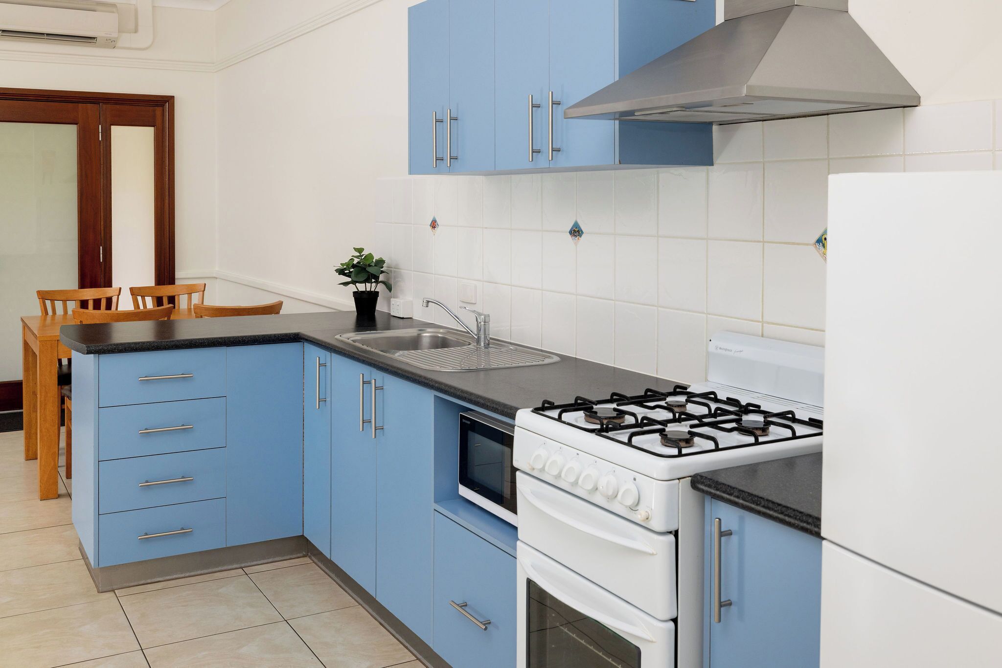 Une cuisine avec des meubles de rangement bleus, une cuisinière à gaz, un évier et un coin repas avec des chaises.