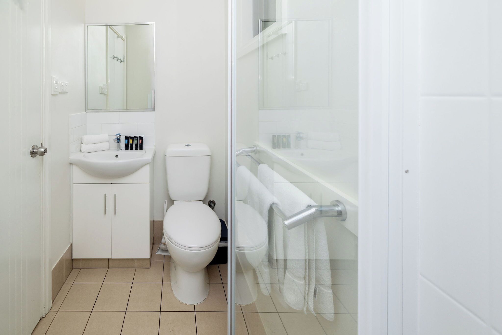 A bathroom with a toilet, sink, and glass shower enclosure.