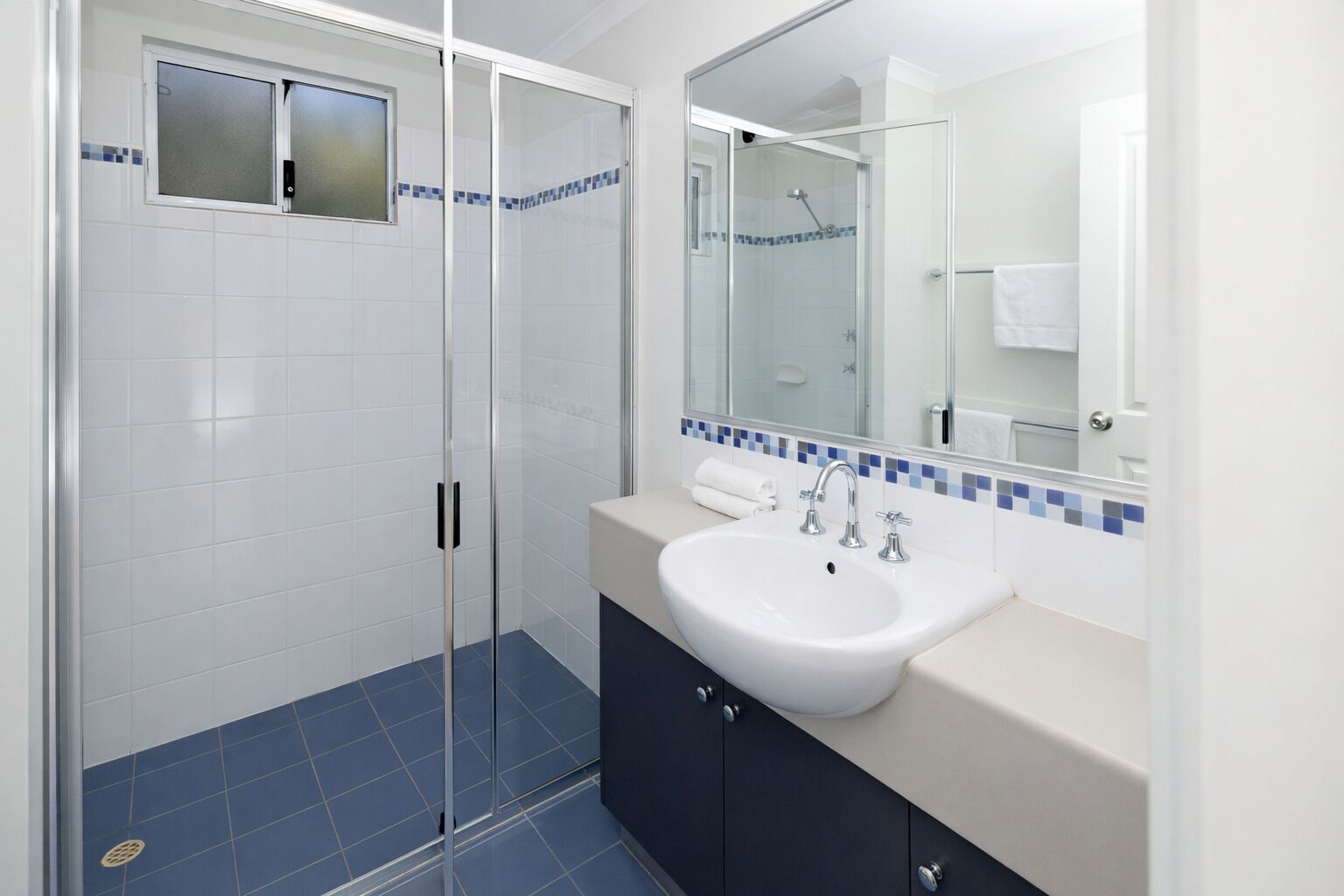 Un baño moderno con cabina de ducha de vidrio, un lavabo blanco y un espejo encima.
