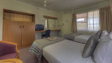A hotel room with two beds, a desk with a computer, a wardrobe, and a window with curtains.