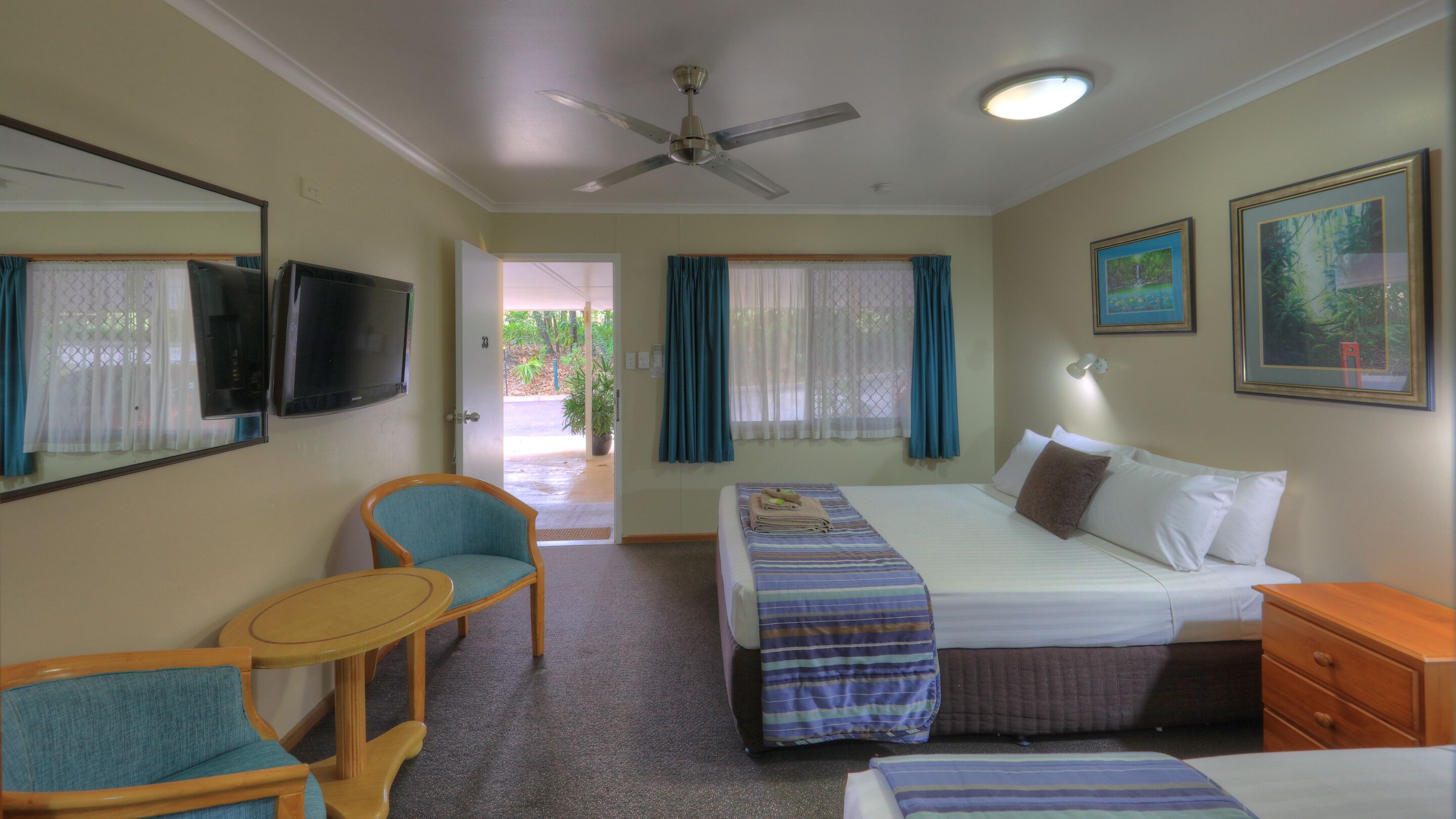 A hotel room with a bed, a chair, a small table, a ceiling fan, and a TV.