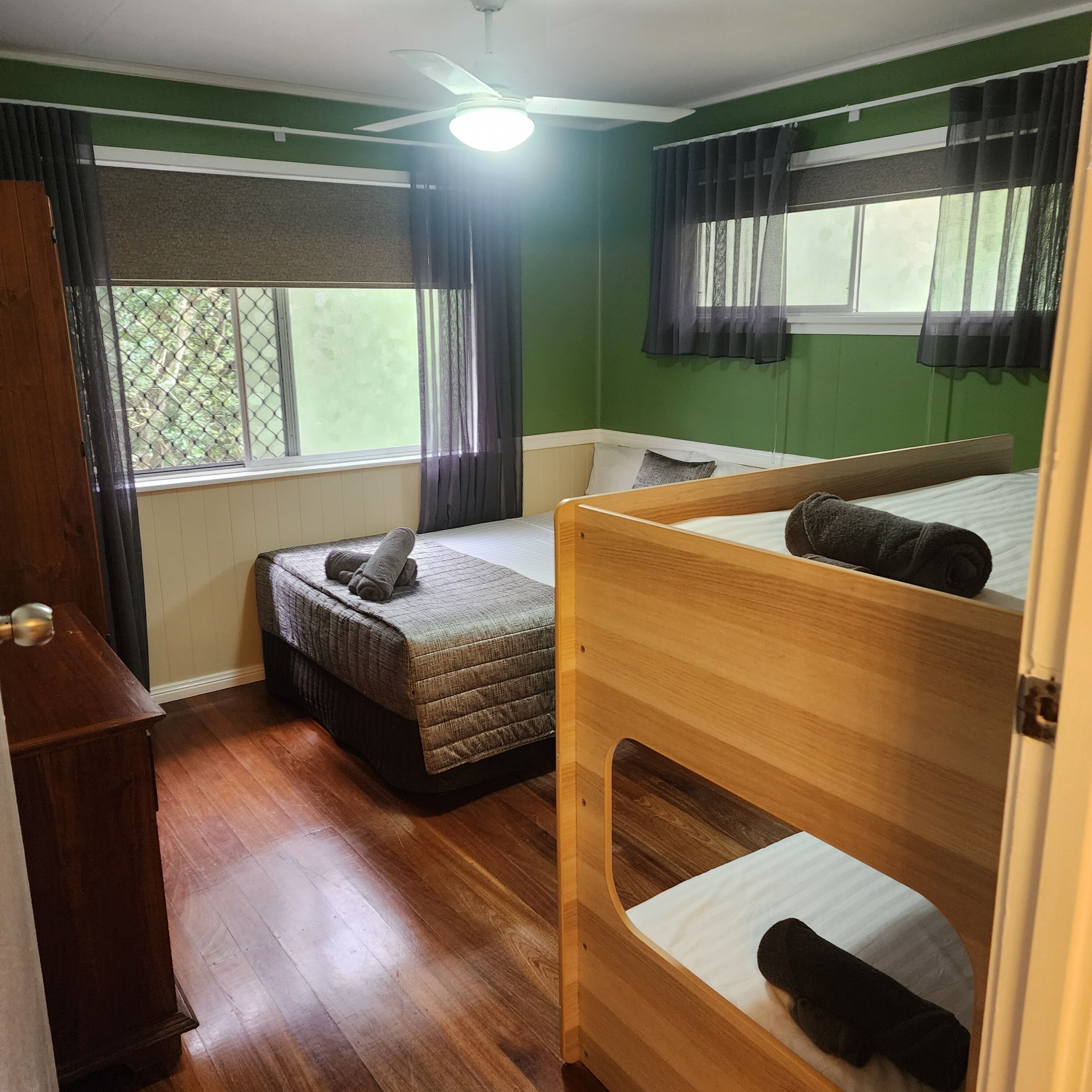 A room with bunk beds, a wooden desk, a window with curtains, and a ceiling fan.