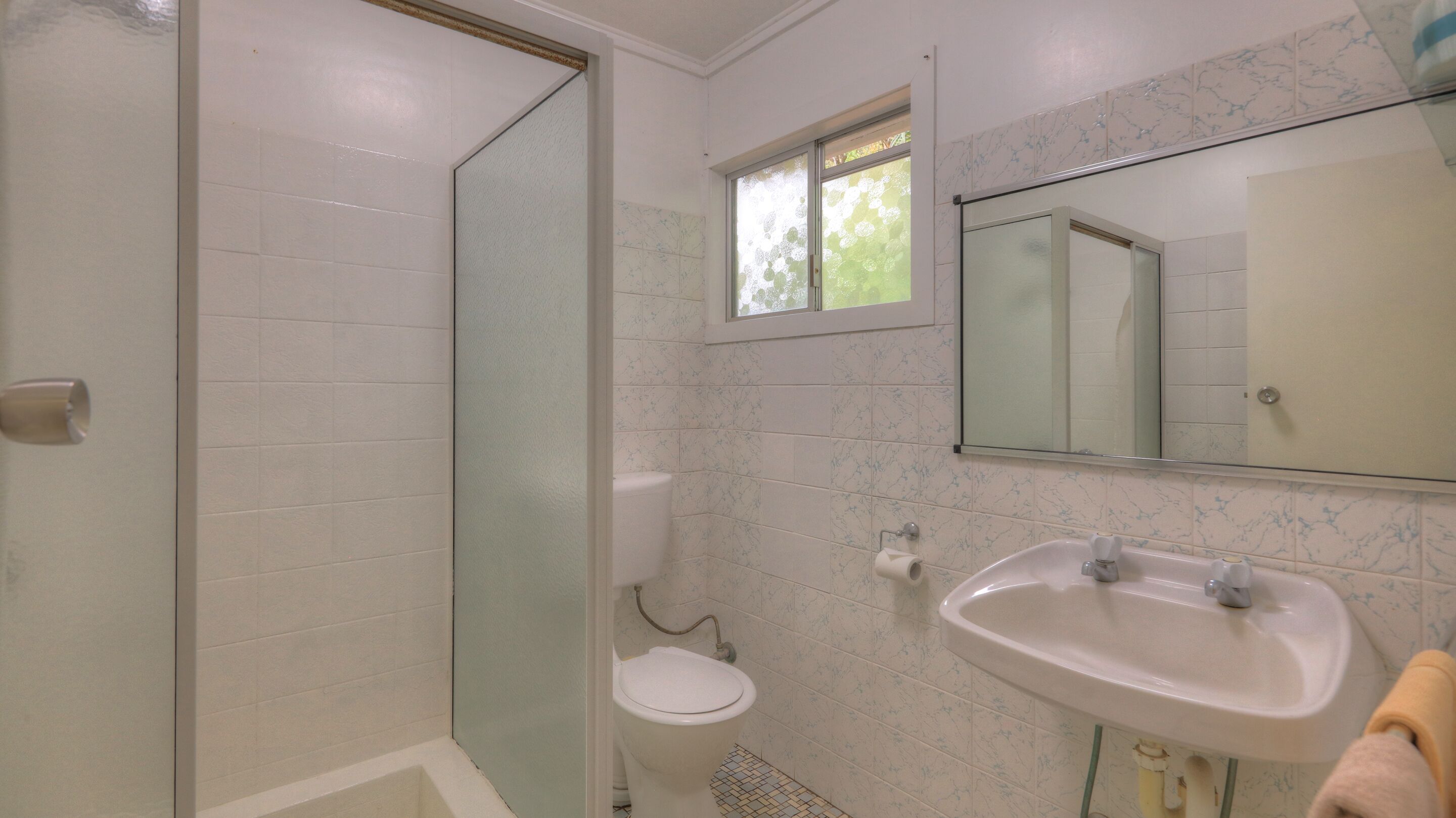 A bathroom with a toilet, sink, and glass shower enclosure.