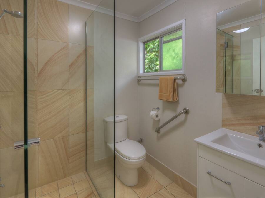 A modern bathroom with a glass shower enclosure, a toilet, a sink, and a window with a view of greenery.