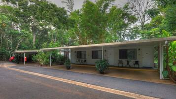 A motel with a covered outdoor seating area, two rooms, and a red car parked outside.