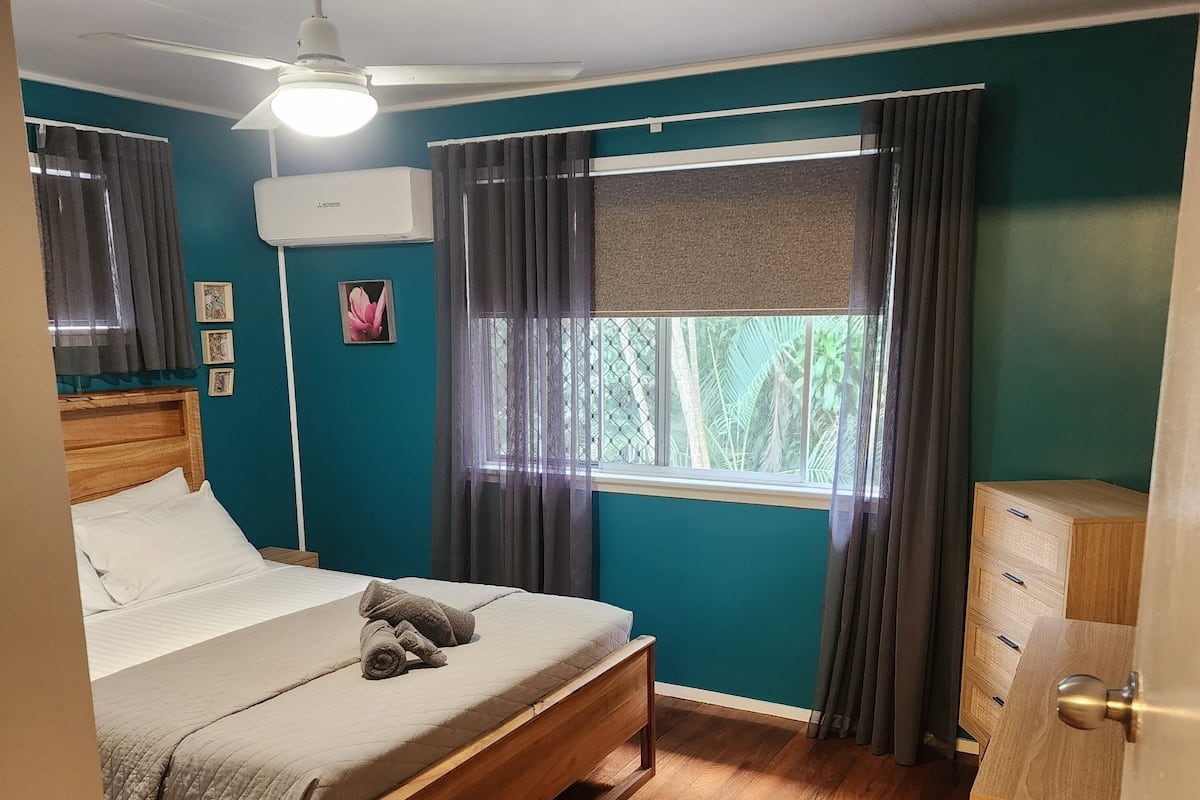 Un dormitorio con cama de madera, ventilador de techo, ventana con cortinas y cómoda de madera.