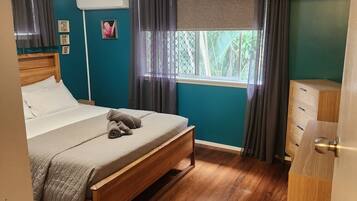 Un dormitorio con cama de madera, ventilador de techo, ventana con cortinas y cómoda de madera.