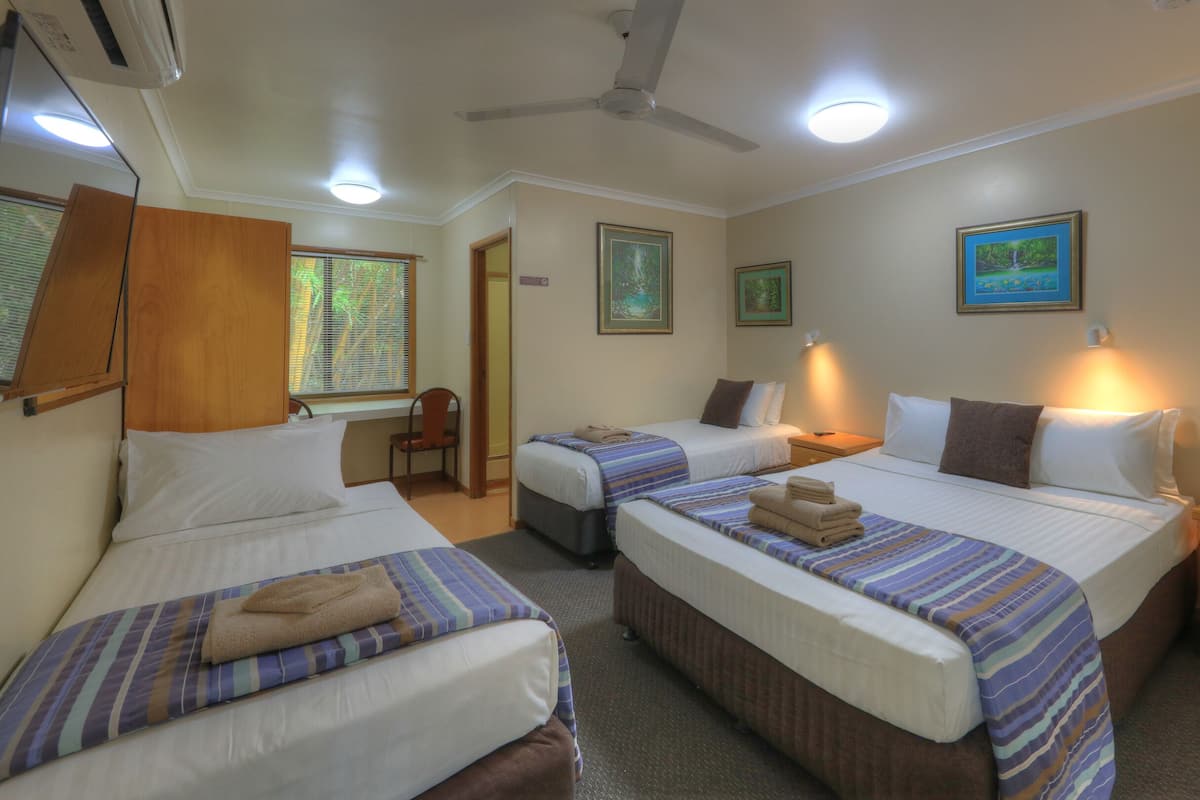 Habitación de hotel con dos camas individuales, una mesita de noche de madera, una silla y una ventana con persianas.
