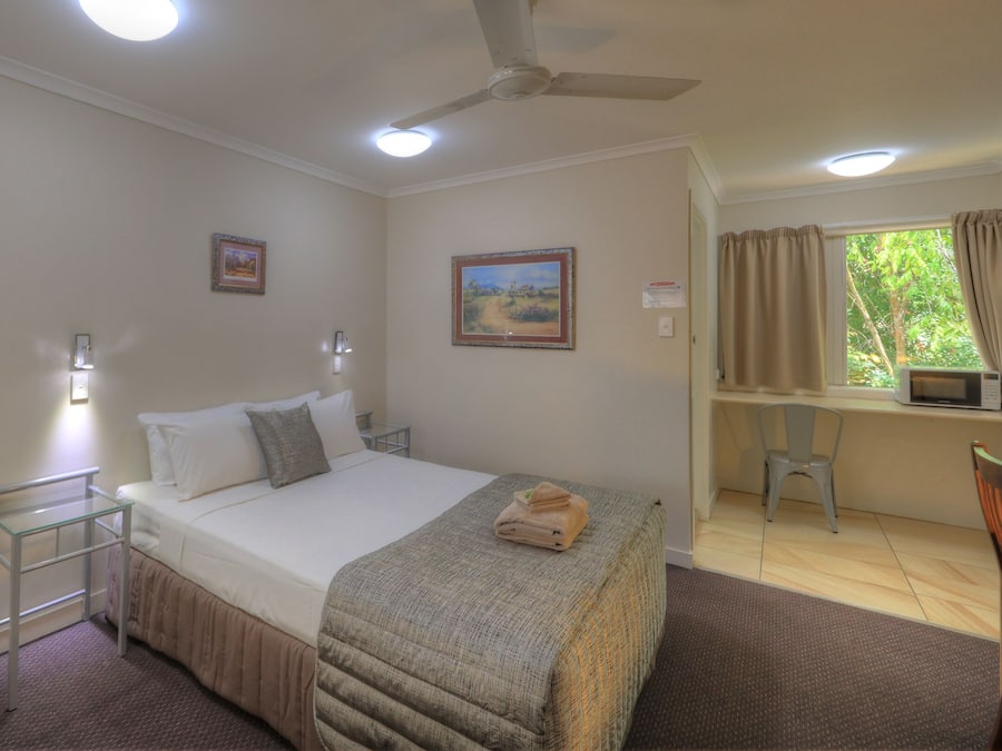 Ein Schlafzimmer mit Bett, Nachttischen, einem Sessel, einem Schreibtisch, einem Deckenventilator und gerahmten Bildern an der Wand.