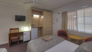 Habitación de hotel con cama, escritorio, silla, mesita, televisor y ventana con cortinas.