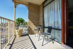 A balcony with a table and chairs, a potted plant, and a view of the street.