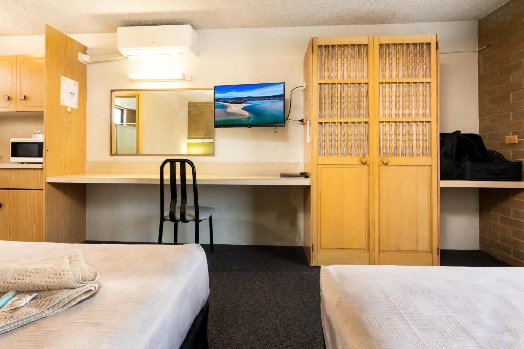Ein Hotelzimmer mit zwei Betten, einem Schreibtisch, einem Stuhl, einem Fernseher und einem Kleiderschrank.