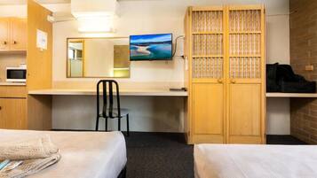 Ein Hotelzimmer mit zwei Betten, einem Schreibtisch, einem Stuhl, einem Fernseher und einem Kleiderschrank.