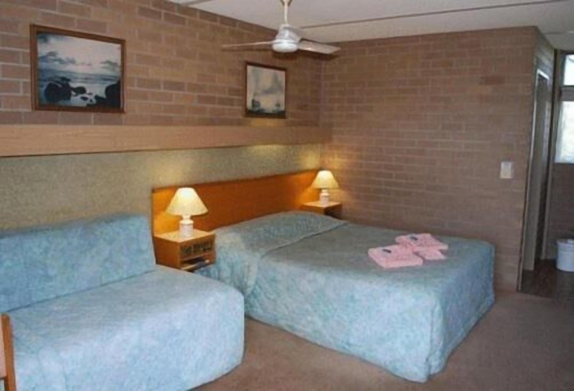Une chambre avec deux lits, chacun doté d’une tête de lit en bois et de lampes de chevet. Deux tableaux sont accrochés au mur, au-dessus des lits.