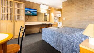 Una habitación de hotel con cama, escritorio, silla, televisor y kitchenette.