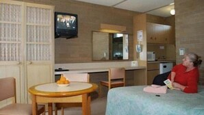A hotel room with a bed, a desk, a chair, a television, and a small table with a bowl of fruit. - Town Centre Motor Inn (Merimbula)