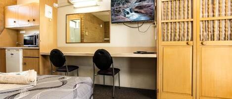 A room with a bed, a desk, two chairs, a television, and a wardrobe.