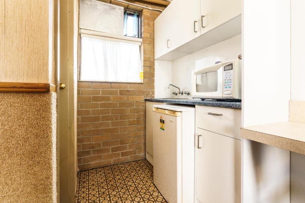 Una cocina compacta con microondas, un lavamanos y una ventana con cortinas.