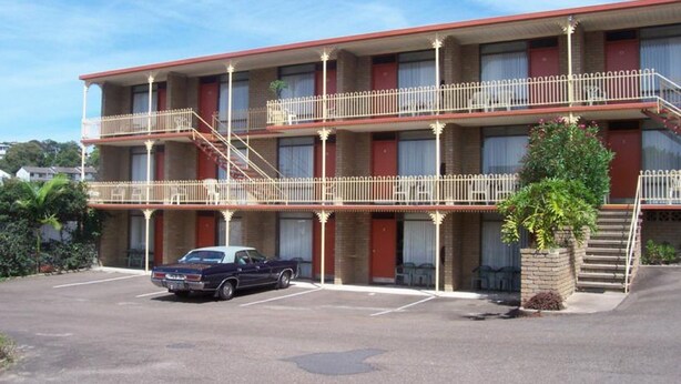 A multi-story motel with a parking lot, a staircase leading to the upper floors, and a single-story building adjacent to it. - Town Centre Motor Inn (Merimbula)