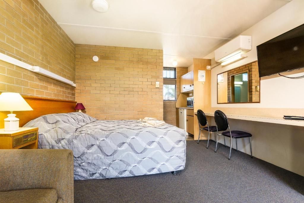 A hotel room with a bed, a desk, a chair, a TV, and a brick wall.