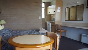 A compact room with a bed, a small kitchenette, a round table with a chair, and a sofa. - Town Centre Motor Inn (Merimbula)