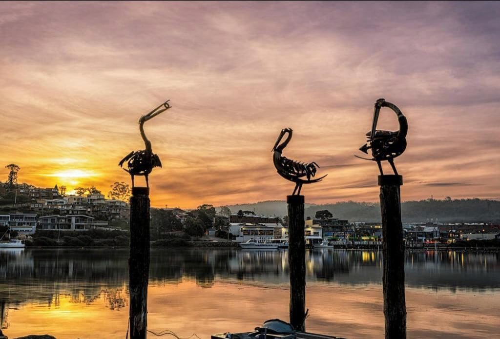 A sunset over a calm lake with three bird sculptures on posts.