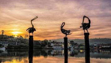 Un atardecer sobre un lago tranquilo con tres esculturas de aves en postes.