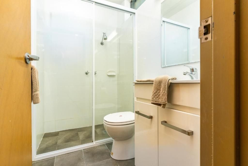 A bathroom with a glass shower enclosure, a toilet, and a sink with a mirror above it.