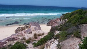 A coastal landscape with a sandy beach, rocky outcrops, and green vegetation. - Town Centre Motor Inn (Merimbula)