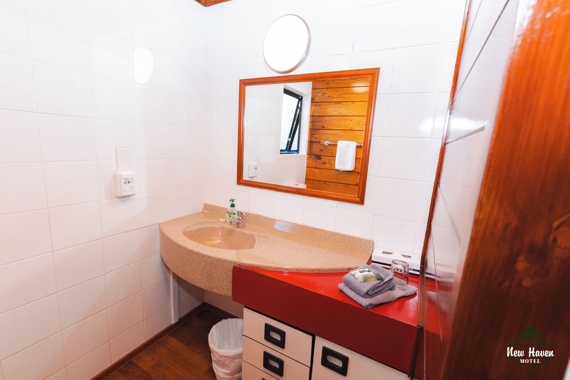 A bathroom with a beige sink, a wooden-framed mirror, and a red countertop.