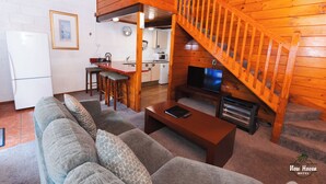 A cozy log cabin interior with a living room, kitchen, and a wooden staircase.