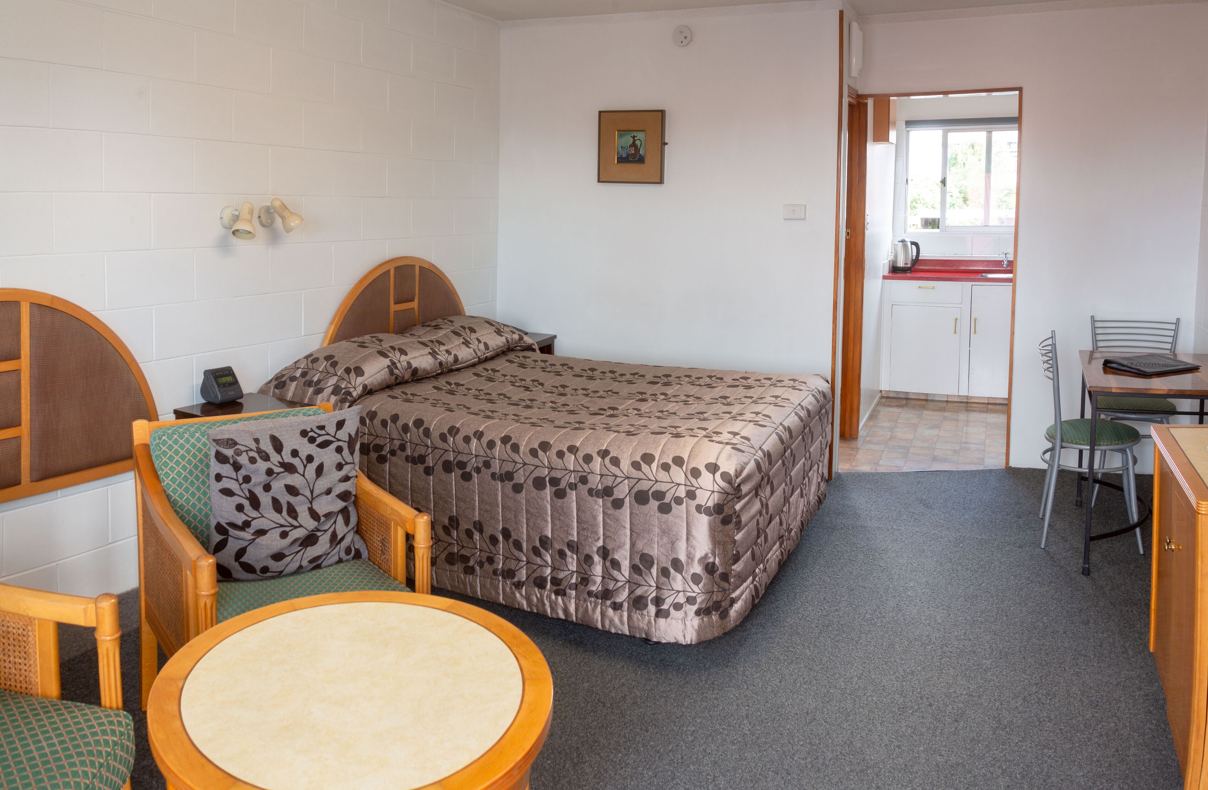 Une pièce de taille modeste comprenant un lit, une petite table, une chaise, un bureau et un coin cuisine.
