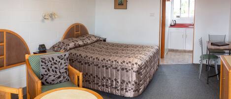 Une pièce de taille modeste comprenant un lit, une petite table, une chaise, un bureau et un coin cuisine.