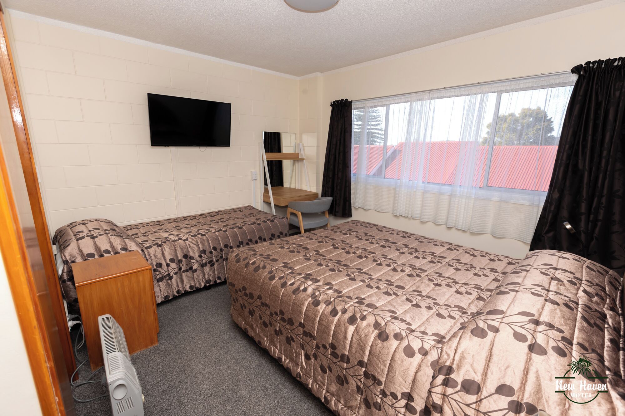 A room with two beds, a TV, a desk, and a window with curtains.