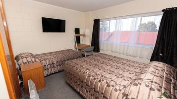 A room with two beds, a TV, a desk, and a window with curtains.