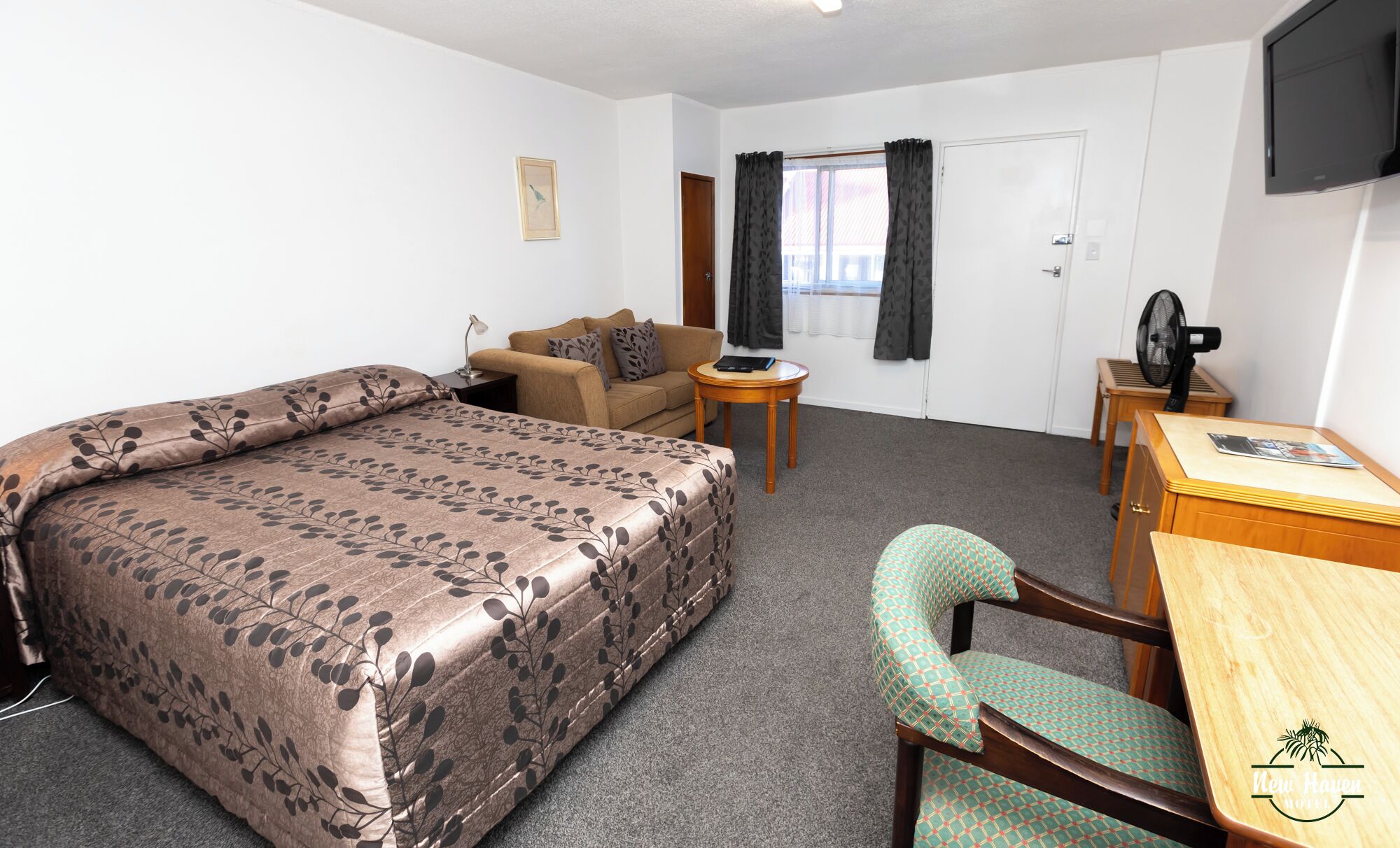 A hotel room with a bed, a sofa, a desk, a chair, a TV, and a window with curtains.