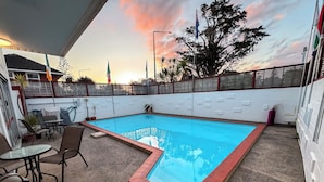 A rectangular pool with a red border, surrounded by outdoor seating and potted plants.