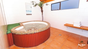 A hot tub with a tiled edge, a wooden bench, a palm plant, and a window.