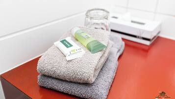 Un baño con encimera roja, una toalla, una botella verde y una caja blanca.