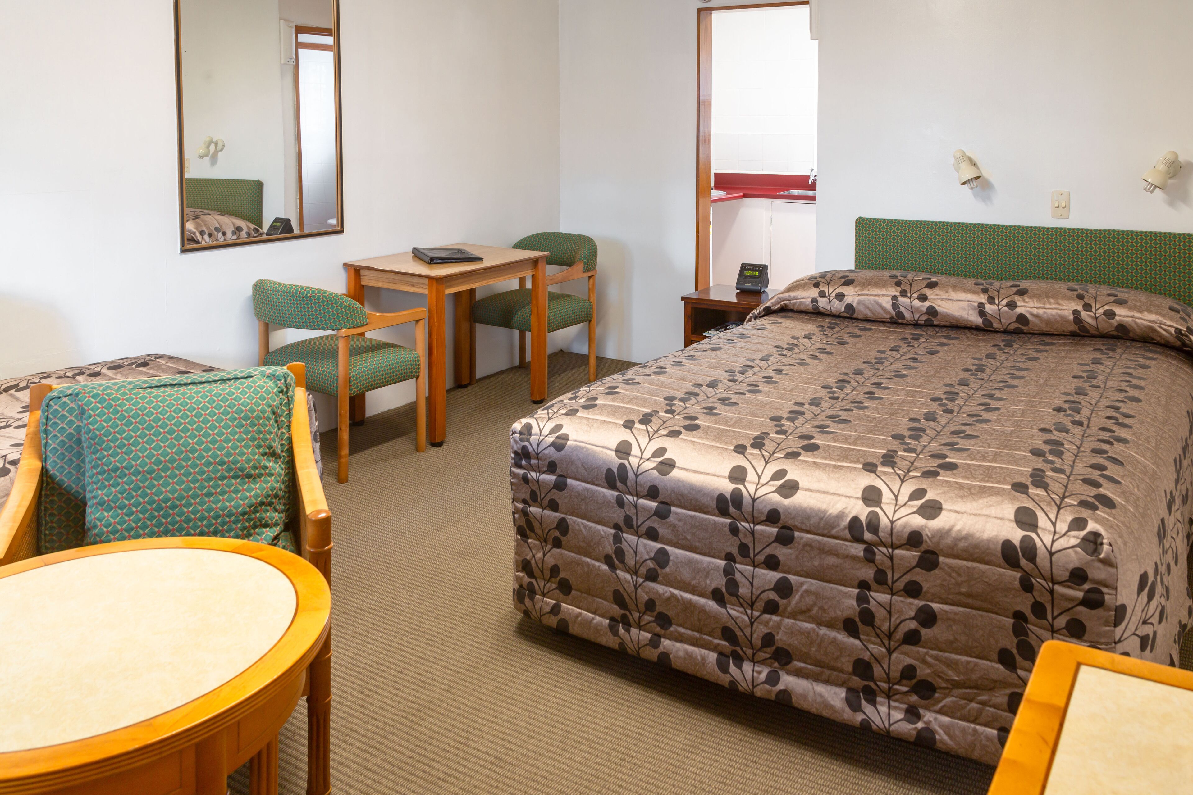 A hotel room with a bed, a desk, two chairs, a round table, and a mirror.