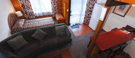Una habitación acogedora con sofá, una mesita, una cama con edredón estampado y una mesa roja.