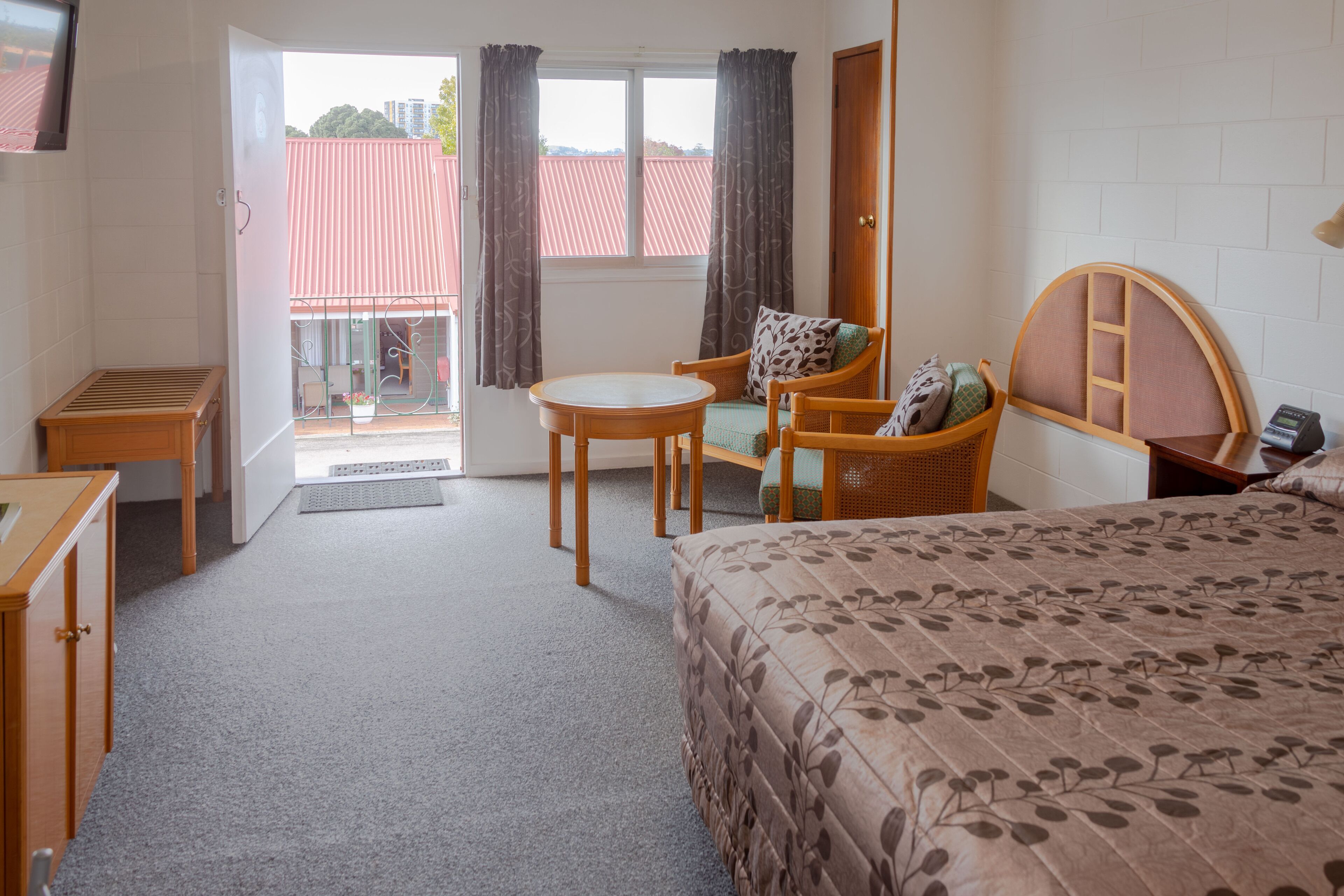 A hotel room with a bed, a chair, a small table, and a window with curtains.